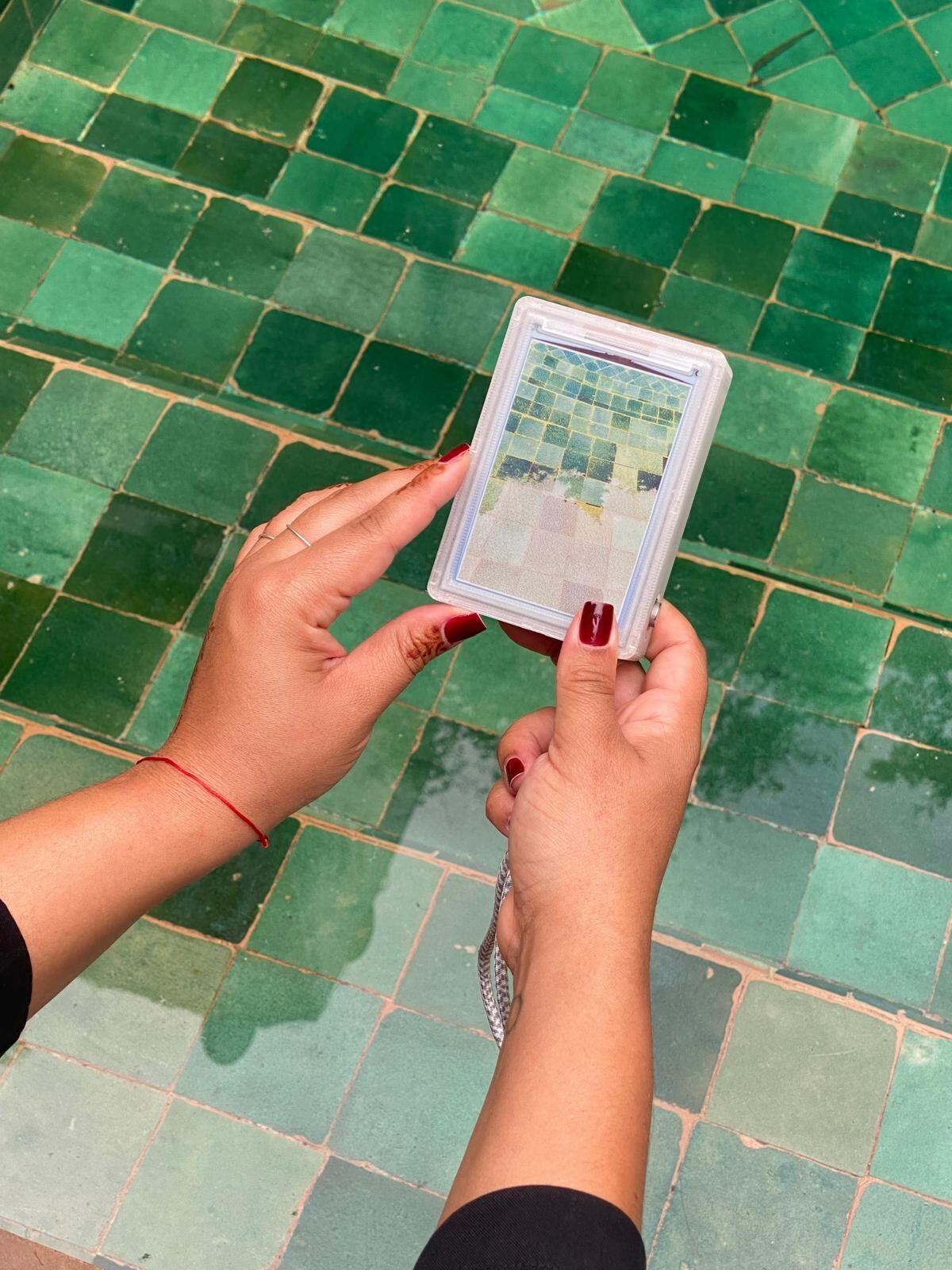 Hands holding reFrame above green tiles, by Denisse Ariana Perez